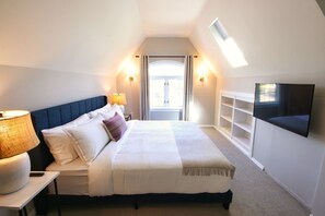 A bedroom with a bed, bedside lamps, a TV, and a window with curtains.