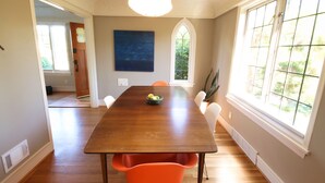 A dining room with a wooden table, orange chairs, and a large window. - Ballard Brick Tudor • A/C • Dog-Friendly (Seattle)