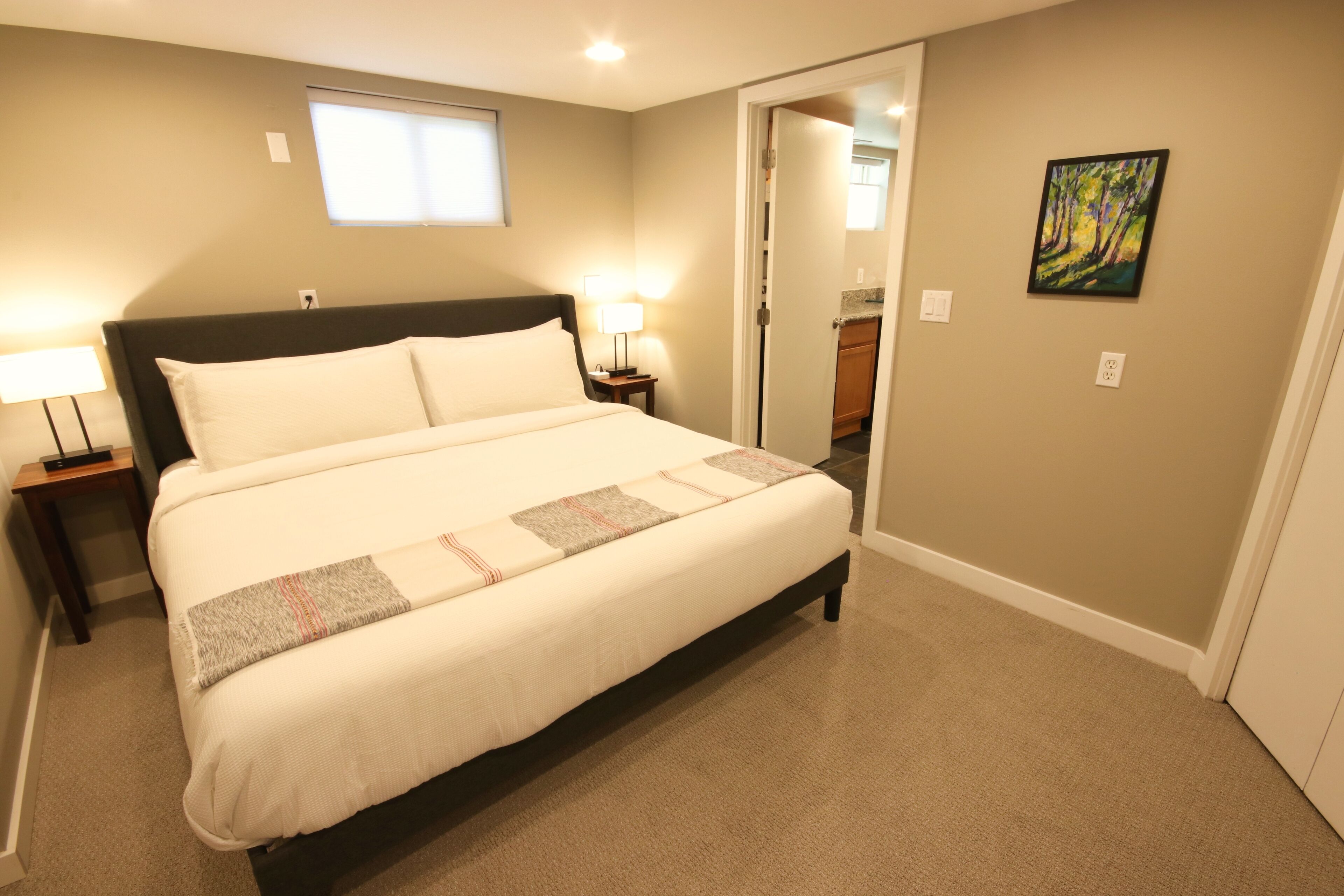 A bedroom with a bed, nightstands, a window, and a painting on the wall.