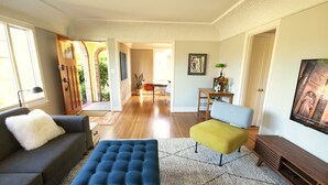 A living room with a sofa, ottoman, and a TV on a wooden stand. - Ballard Brick Tudor • A/C • Dog-Friendly (Seattle)