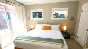 A bedroom with a large bed, two bedside lamps, a window, and a door. - Ballard Brick Tudor • A/C • Dog-Friendly (Seattle)