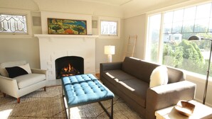 A living room with a fireplace, a sofa, a chair, a coffee table, and a view of the outdoors. - Ballard Brick Tudor • A/C • Dog-Friendly (Seattle)