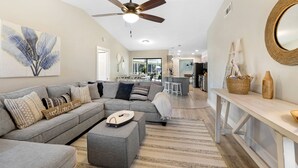 A modern living room with a grey sectional sofa, a ceiling fan, and a large abstract painting. - Billiards and Poolside Bliss Centrally located in SE Cape Coral, Pet Friendly! (Cape Coral)