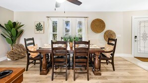 A dining area with a wooden table and chairs, a ceiling fan, and a view through windows. - Billiards and Poolside Bliss Centrally located in SE Cape Coral, Pet Friendly! (Cape Coral)