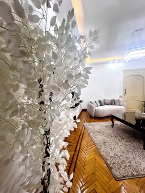 Un soggiorno con un divano bianco, un tappeto decorato e una pianta bianca ornamentale.
