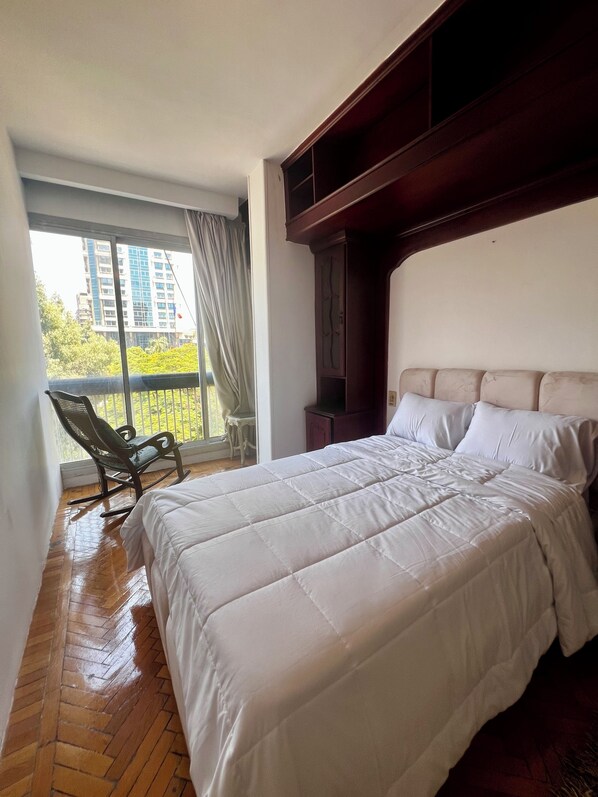 Una camera da letto con un letto grande, una poltrona a dondolo e un balcone con vista sugli edifici.