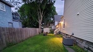 A backyard with a wooden fence, a tree, and a house with a stone foundation. - Single level 3 bedroom, fenced yard, central air (Auburn)