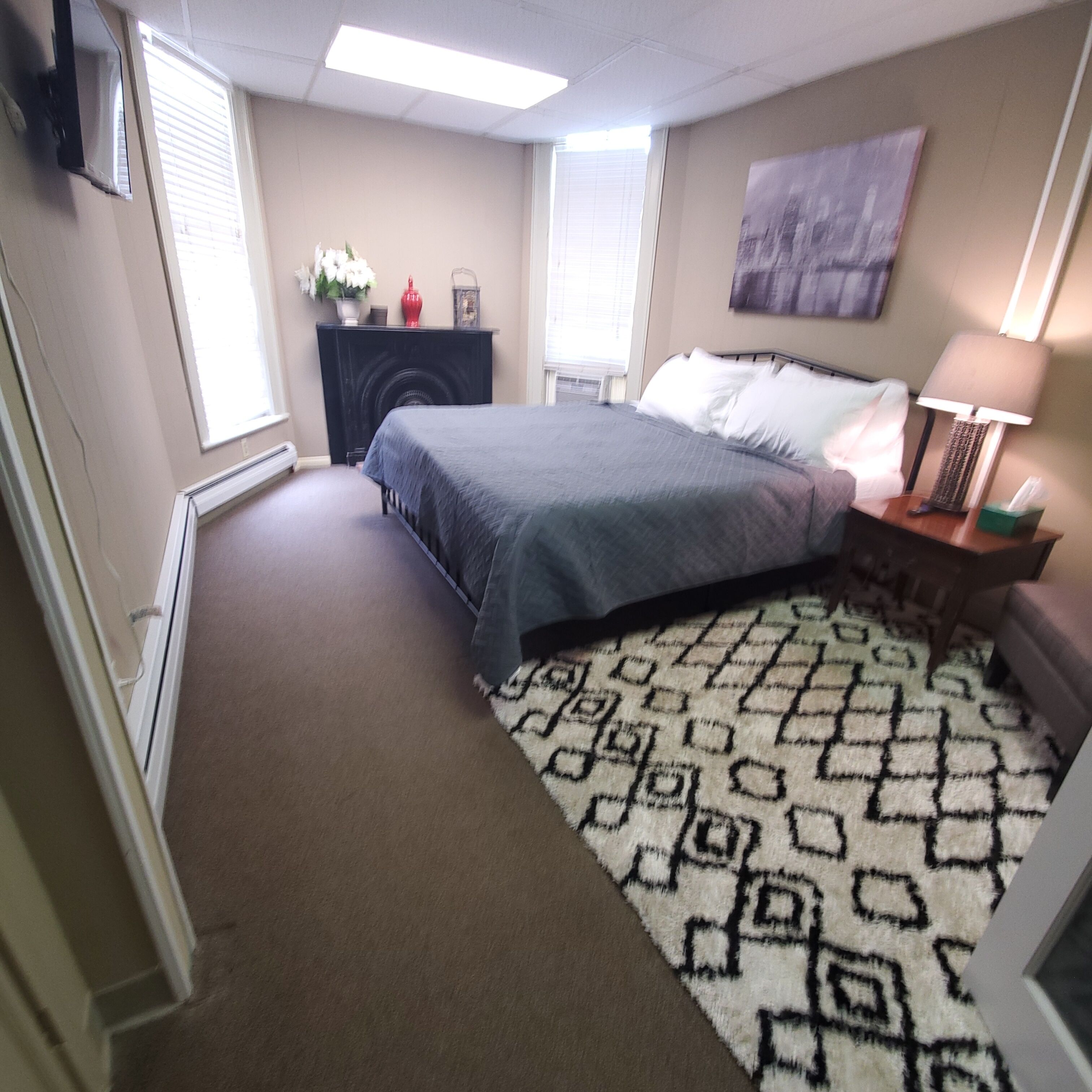 Un dormitorio con una cama, una mesita de noche, una lámpara, un radiador y una ventana.