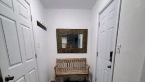 Un couloir étroit avec des portes blanches, un banc en bois, un tapis noir et un luminaire au plafond.