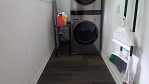 Une buanderie équipée de deux machines à laver superposées, d’un étendoir et d’un balai appuyé contre le mur.