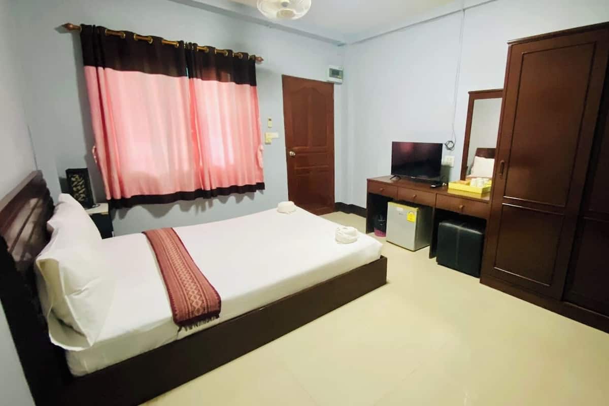 A hotel room with a bed, a desk with a television, a wardrobe, and a window with curtains.