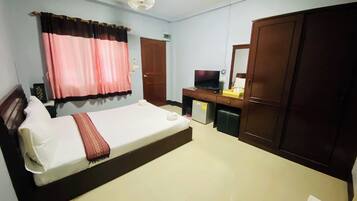 A hotel room with a bed, a desk with a television, a wardrobe, and a window with curtains.