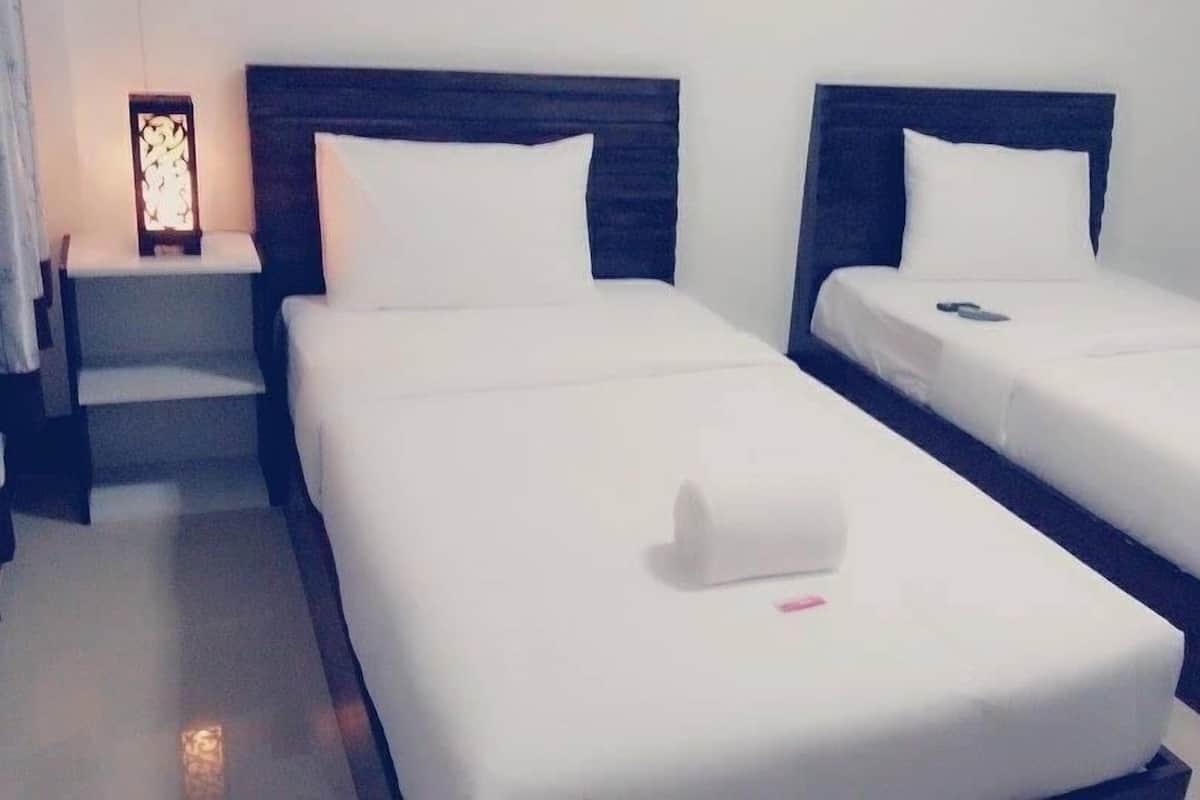 A hotel room with two single beds, each with a wooden headboard, white linens, and a small bedside table with a lamp.