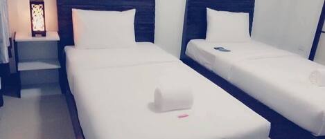 A hotel room with two single beds, each with a wooden headboard, white linens, and a small bedside table with a lamp.