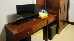 Une pièce de taille modeste, comprenant un bureau en bois, un petit réfrigérateur, une poubelle et une armoire.