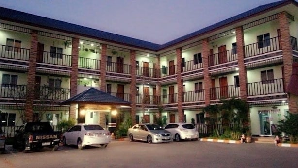 Un hôtel à plusieurs étages doté d’une cour intérieure, avec des balcons à chaque étage et plusieurs voitures garées devant.