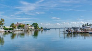 Um areal tranquilo com um cais, barcos e casas ao fundo.