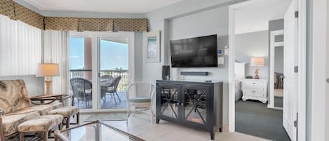 Una sala de estar amplia con ventilador de techo, televisor de pantalla plana, comedor con mesa de vidrio y balcón con mobiliario exterior.