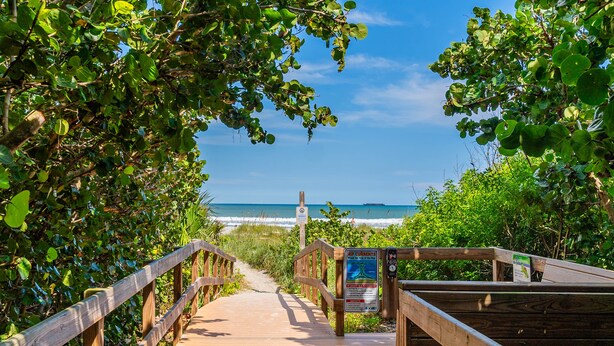 A wooden boardwalk leading to a beach with a signboard.