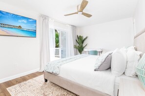 Une chambre à coucher avec un lit, un ventilateur de plafond, une fenêtre avec des rideaux, une plante et une vue sur une jetée.