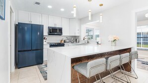 A modern kitchen with white cabinets, a blue refrigerator, a central island with bar stools, and pendant lighting.
