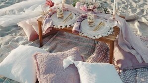 A beach picnic setup with a table, candles, and a blanket.