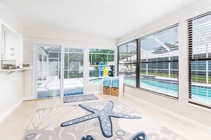 Une pièce lumineuse et ensoleillée, avec un grand tapis en forme d’étoile de mer, une vue sur la piscine et un espace de rangement contenant des serviettes.