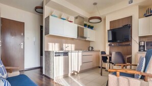 Un espai habitable compacte amb petita cuina, zona de menjador i zona d'estar amb sofà i butaca.