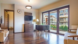Un apartament modern amb terres de fusta, televisió de pantalla plana, zona de menjador i finestres grans amb vista a la ciutat.
