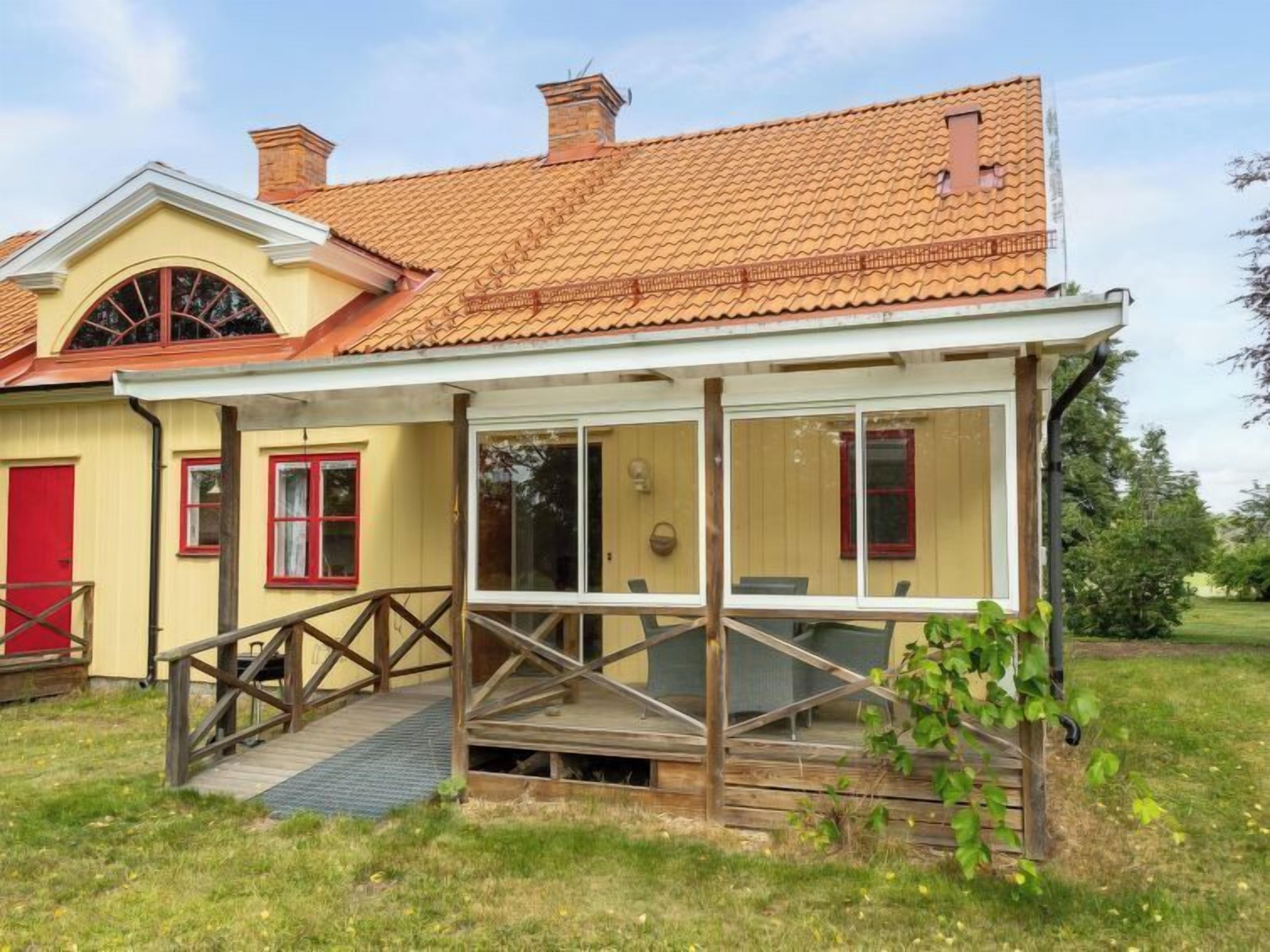 A two-story house with a covered porch, a red door, and a small garden area.