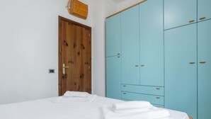 A bedroom with a wooden door, a large blue wardrobe, and a neatly made bed with folded white towels. - Acquamarina Gaia by Interhome (San Vito lo Capo)