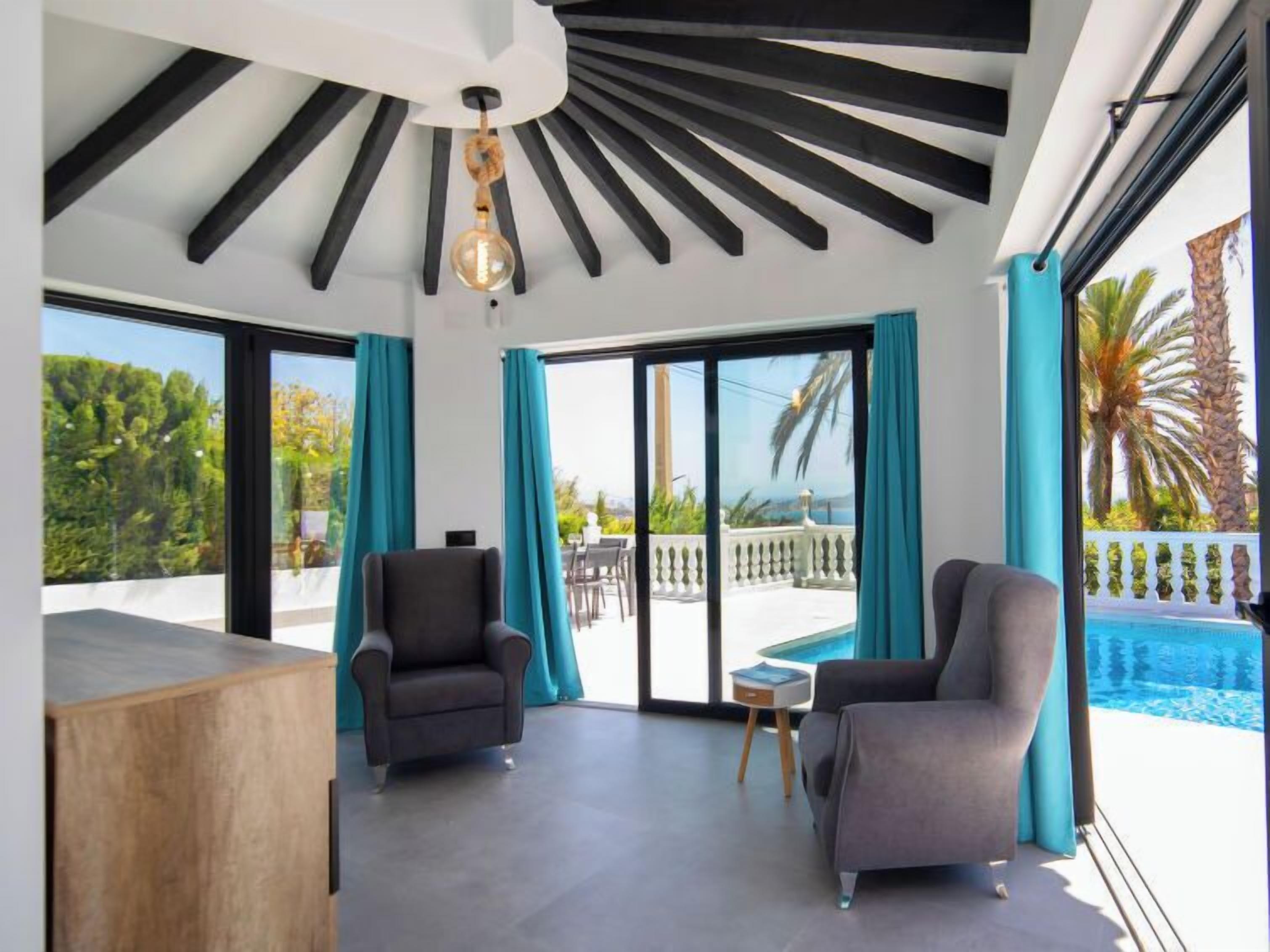 A modern room with a pool, two armchairs, and a ceiling with black beams and a hanging light fixture.