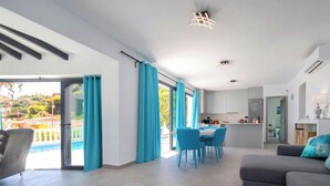 A modern living room with a grey sofa, a dining area with blue chairs, and a kitchen in the background. - Estrella Azul by Interhome (Calpe/Calp)