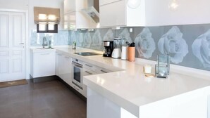 A modern kitchen with white cabinetry, a central island, and a backsplash with floral patterns. - Limoneros by Interhome (Nerja)