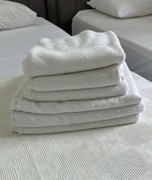 Una pila de toallas blancas sobre una cama con una colcha blanca texturizada.