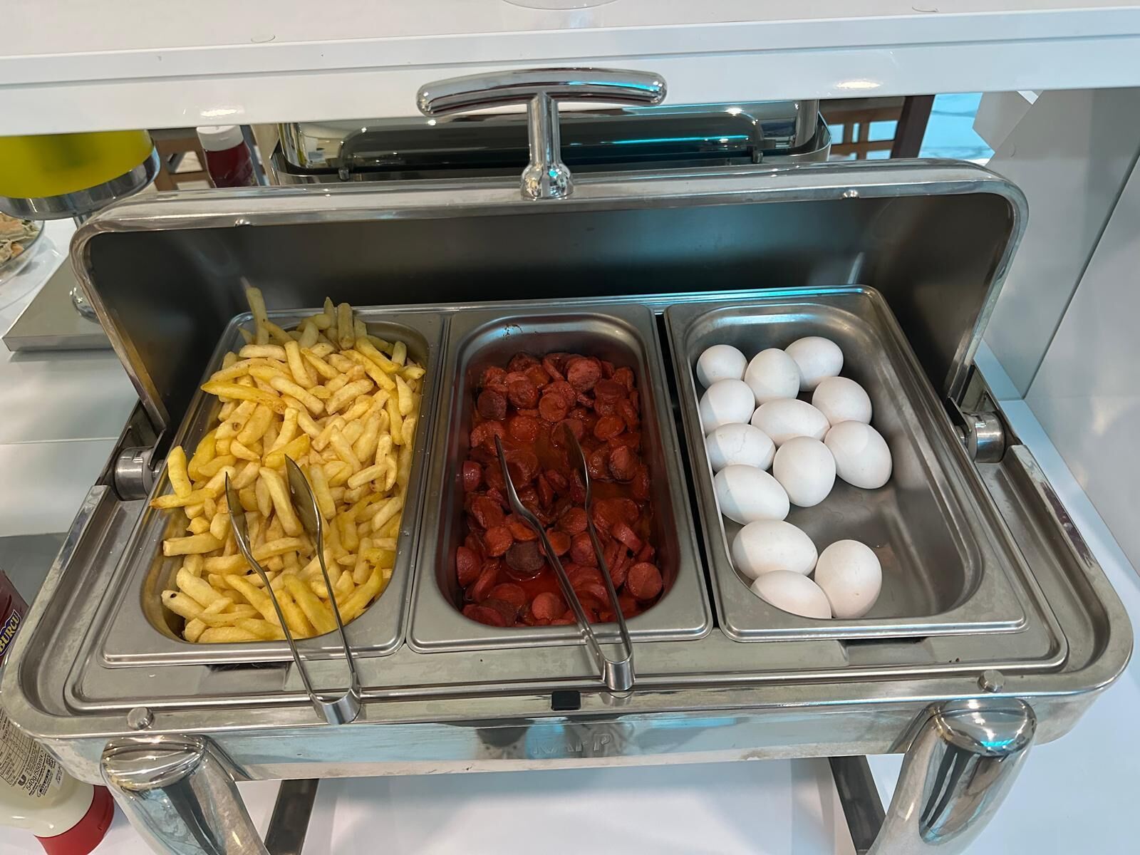 A buffet with French fries, sausage slices, and eggs.