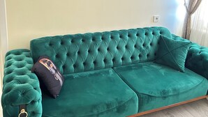 Un sofá tapizado en color verde azulado con diseño capitonado, colocado frente a una pared de color claro con tres obras de arte decorativas.