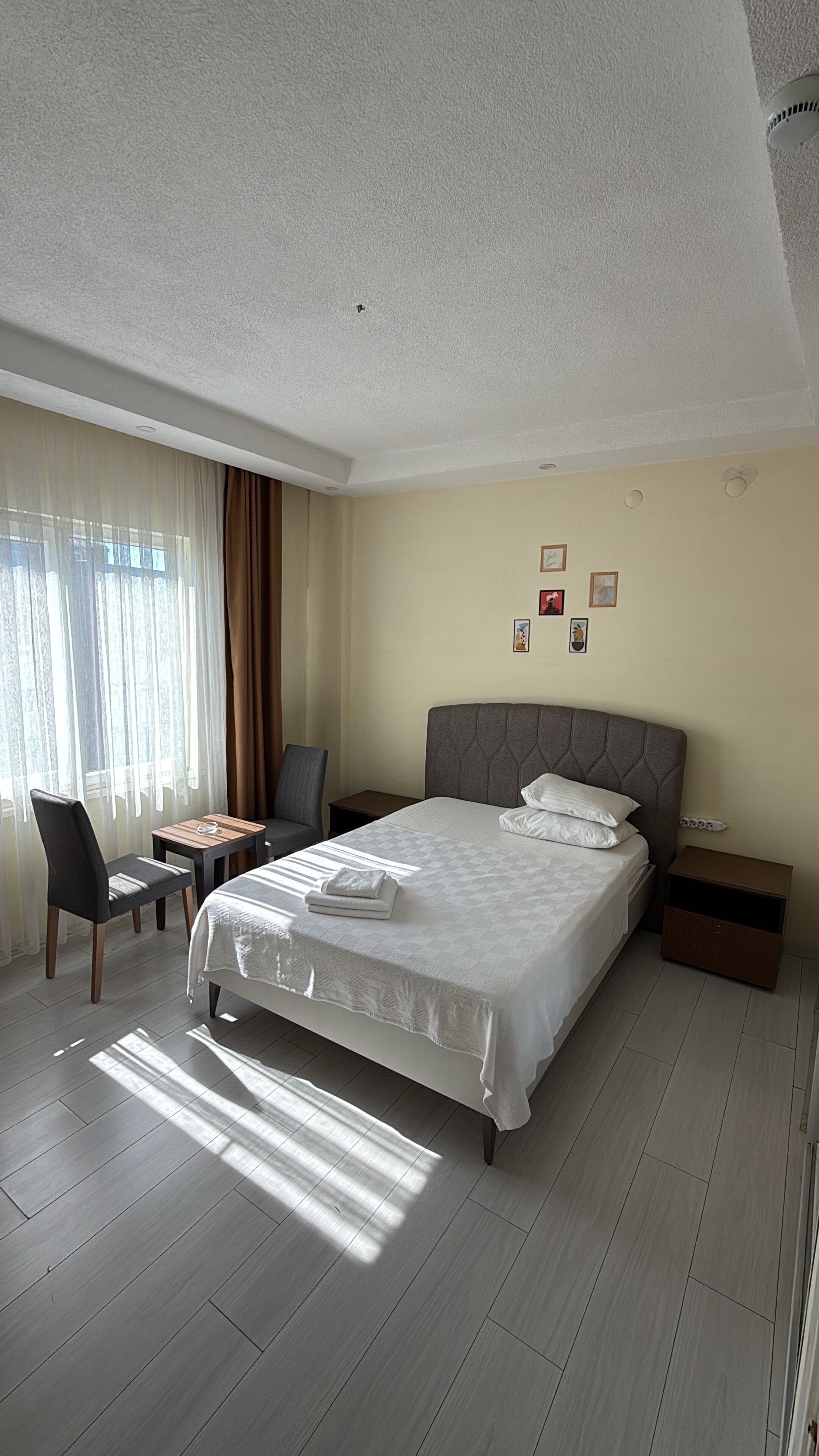 Quarto de hotel com cama, cadeira, mesa pequena e criado-mudo.