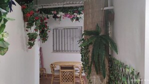 A small, enclosed outdoor area with a table and chairs, surrounded by lush greenery and flowering plants.