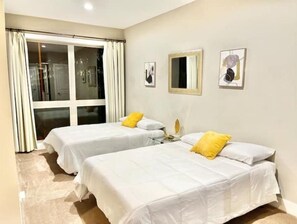 Two single beds with white bedding and a single pillow each, complemented by framed artworks and a large window with curtains.