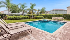 A rectangular swimming pool with a hot tub, surrounded by a brick patio and lounge chairs.