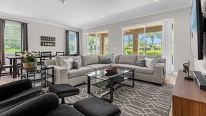 A modern living room with a sectional sofa, a glass coffee table, and a dining area with a table and chairs.