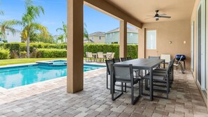 A covered outdoor area with a pool, a table with chairs, and a ceiling fan.