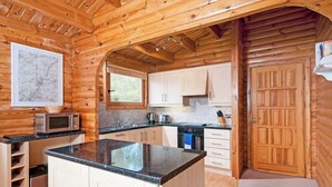 A wooden cabin interior with a kitchen featuring a central island, cabinets, a microwave, and a stove.
