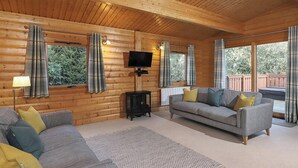 A log cabin interior with a sofa, a television, and a wood-burning stove.