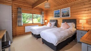 A wooden cabin bedroom with two beds, a window with curtains, and a radiator.