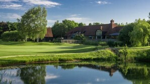 A golf course with a pond reflecting the clubhouse and trees.