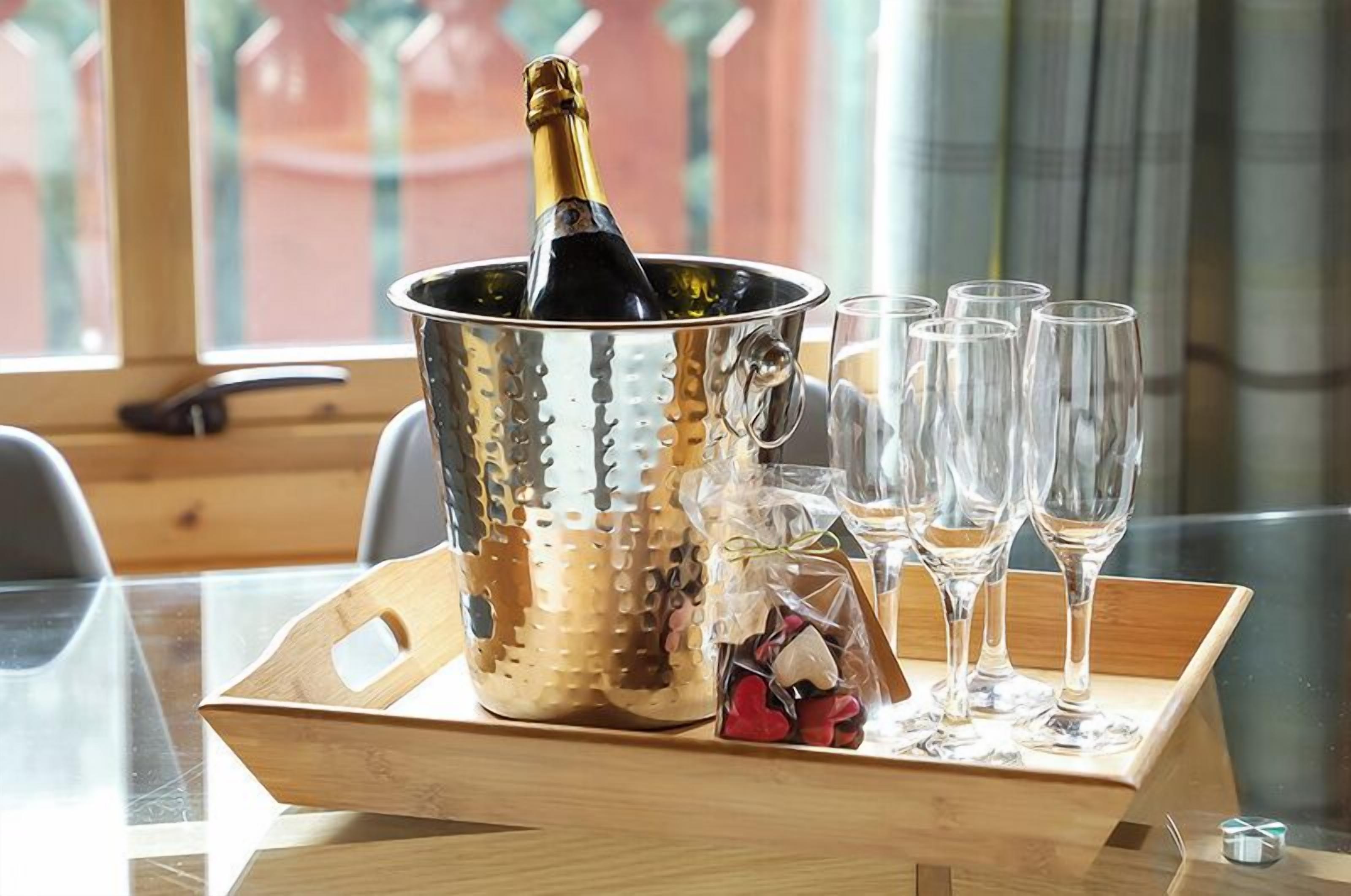 A metallic champagne bucket with a bottle, surrounded by empty glasses on a wooden tray.