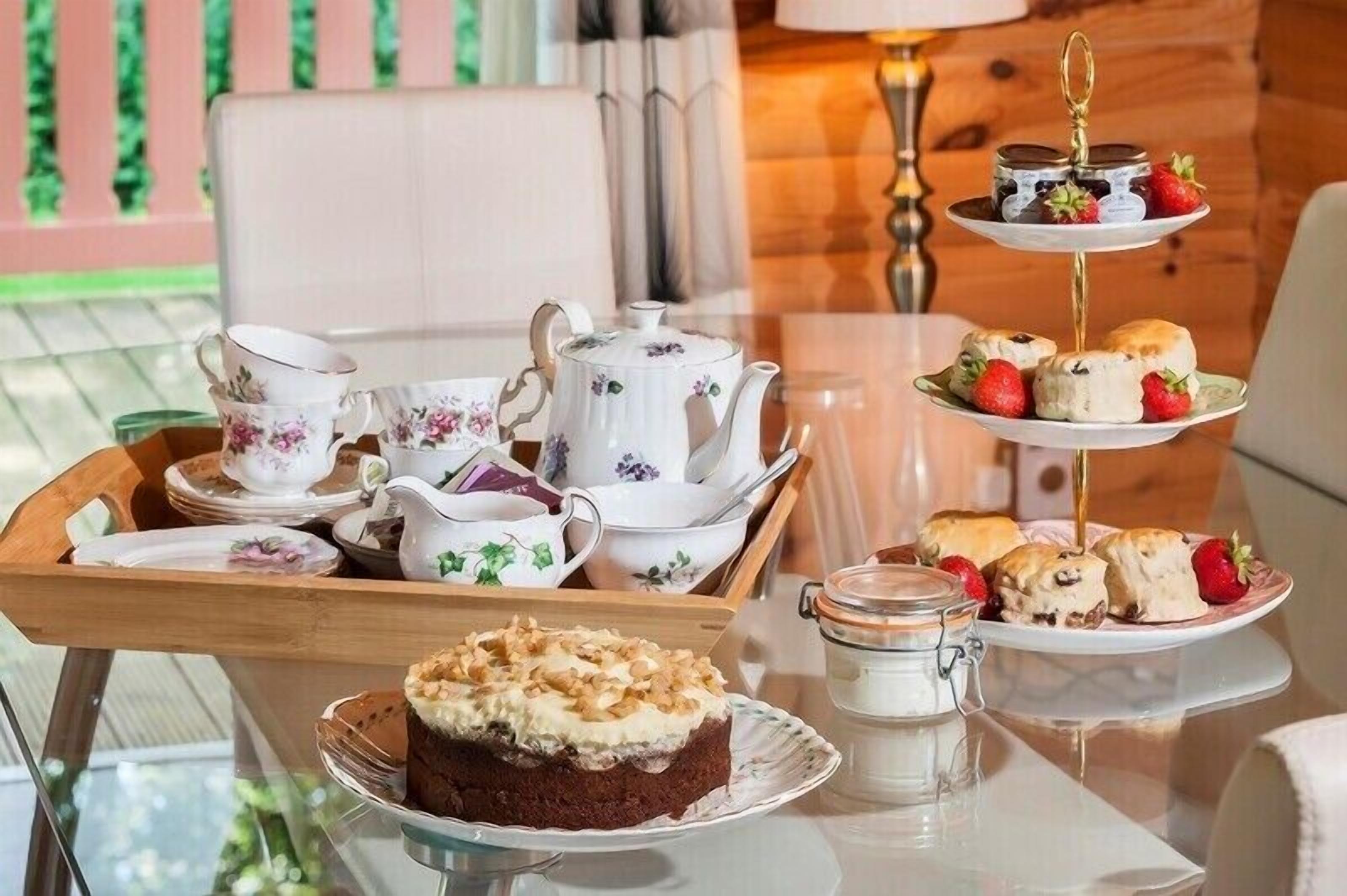 A tea service set with a teapot, cups, saucers, and a tray with pastries and a cake.