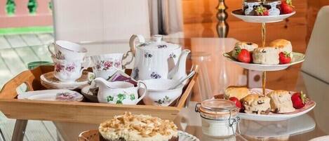 A tea service set with a teapot, cups, saucers, and a tray with pastries and a cake.